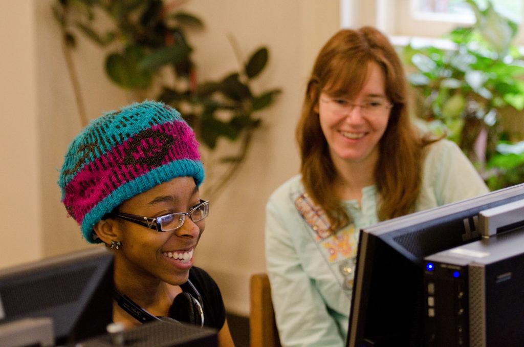 A student and a teacher looking at a computer working together